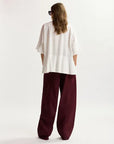 Person wearing a white top and burgundy pants on a light background