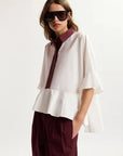 Woman wearing a white blouse with burgundy accents and sunglasses on a white background