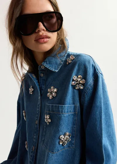 Person wearing a blue denim jacket with decorative pins on a plain background
