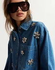 Person wearing a blue denim jacket with decorative pins on a plain background