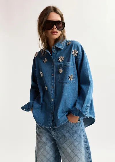 Person wearing a blue denim jacket with floral embellishments on a white background