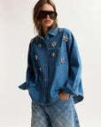 Person wearing a blue denim jacket with floral embellishments on a white background