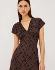 A woman modeling a dark brown midi wrap dress with a textured abstract pattern, short flutter sleeves, and a V-neckline, against a plain white studio background.
