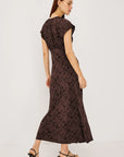 A woman modeling a dark brown midi dress with a black abstract pattern, shown from a rear three-quarter angle against a plain white studio background.