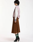 A model is shown from a side profile wearing a pink and white striped button-up shirt, a brown midi skirt, green and white striped socks, and black ankle boots, set against a plain white studio background.
