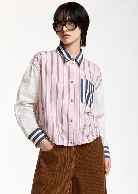 A model wearing a pink and white vertically striped button-up shirt with navy blue striped accents on the collar, cuffs, and chest pocket, paired with brown corduroy pants and black sunglasses, against a plain white background.