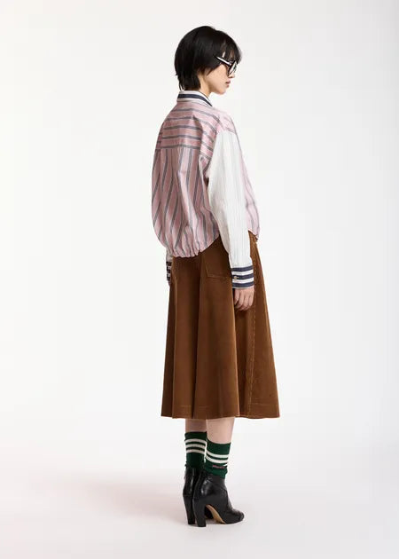 A model is shown from the back wearing a pink and white striped jacket over a white shirt, paired with a brown corduroy skirt, green and white striped socks, and black leather ankle boots, against a plain white studio background.