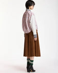A model is shown from the back wearing a pink and white striped jacket over a white shirt, paired with a brown corduroy skirt, green and white striped socks, and black leather ankle boots, against a plain white studio background.