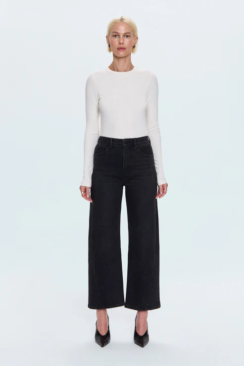 Person wearing a white long-sleeve top and black wide-leg jeans on a light blue background