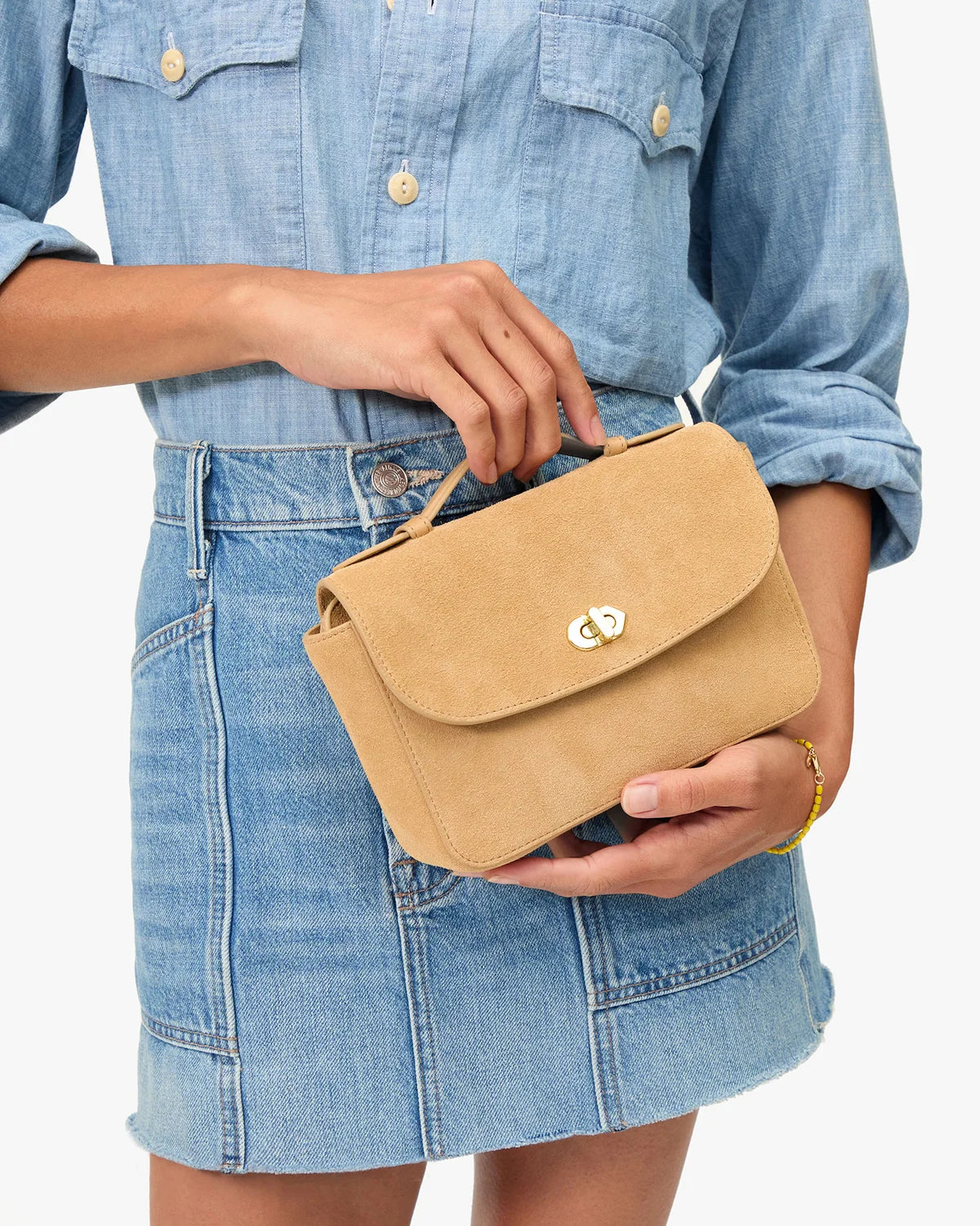 Person holding a tan handbag wearing a denim outfit on a white background