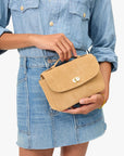 Person holding a tan handbag wearing a denim outfit on a white background