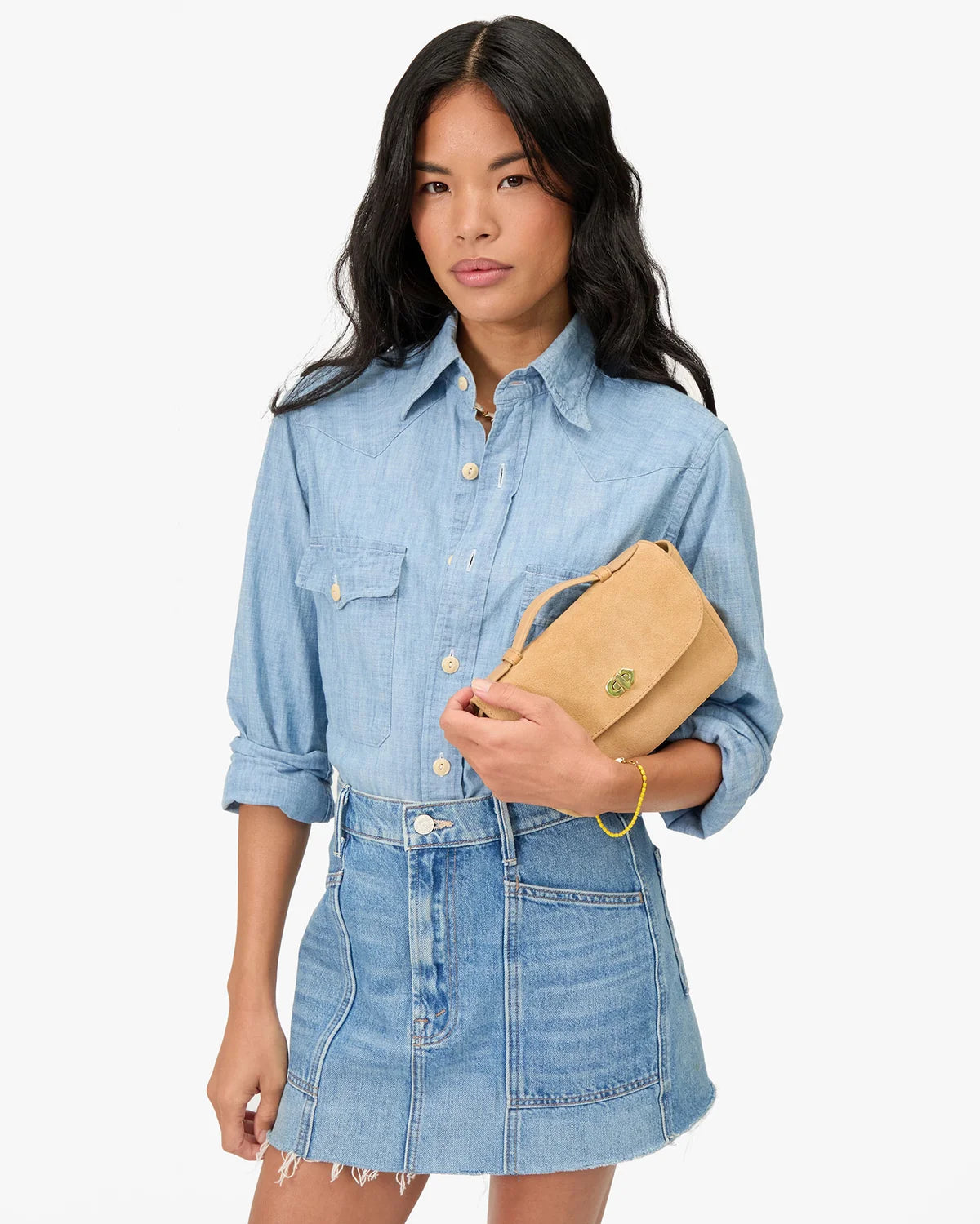 Woman wearing a denim outfit holding a beige handbag on a white background