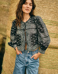 Woman wearing a black patterned blouse and blue jeans standing against hay bails.