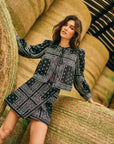 Woman in a black and white patterned outfit standing next to hay bales.