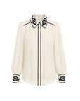 An off-white long-sleeve blouse with black embroidered geometric patterns on the pointed collar, cuffs, and down the center front placket, shown against a plain white background.