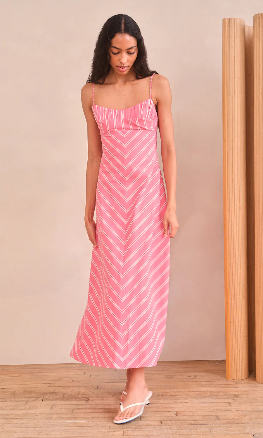 Woman wearing a pink and white striped dress against a beige wall.