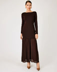 A woman modeling a dark brown long-sleeve maxi dress with a boat neckline and a pleated skirt, standing against a light gray studio background.
