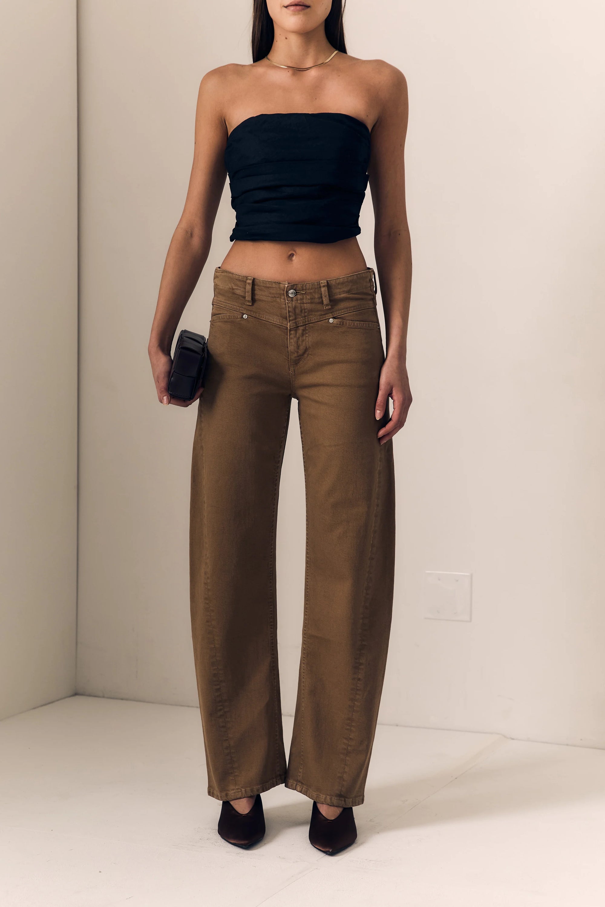 Woman wearing a black strapless top and brown wide-leg pants against a plain background