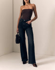 model wearing a strapless brown top with dark jeans on a cream background 