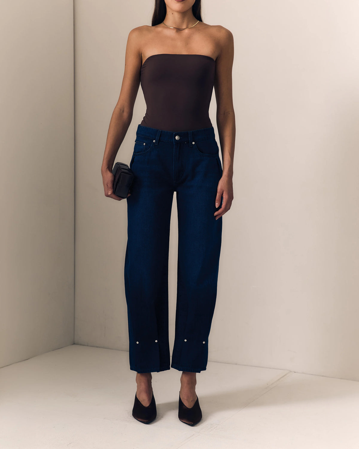model wearing dark blue jeans with a pinched hem and a strapless brown top on a cream background 