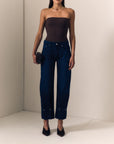 model wearing dark blue jeans with a pinched hem and a strapless brown top on a cream background 