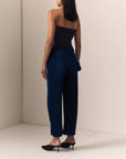 model wearing dark blue jeans with a pinched hem and a strapless brown top on a cream background, back view