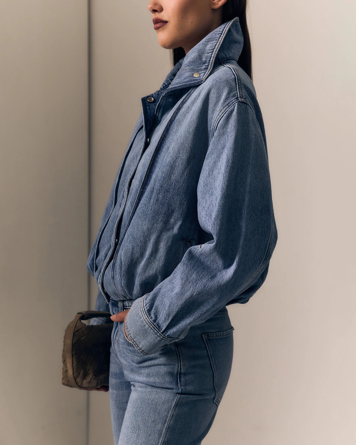 model wearing a denim jacket with jeans on a cream background, side view