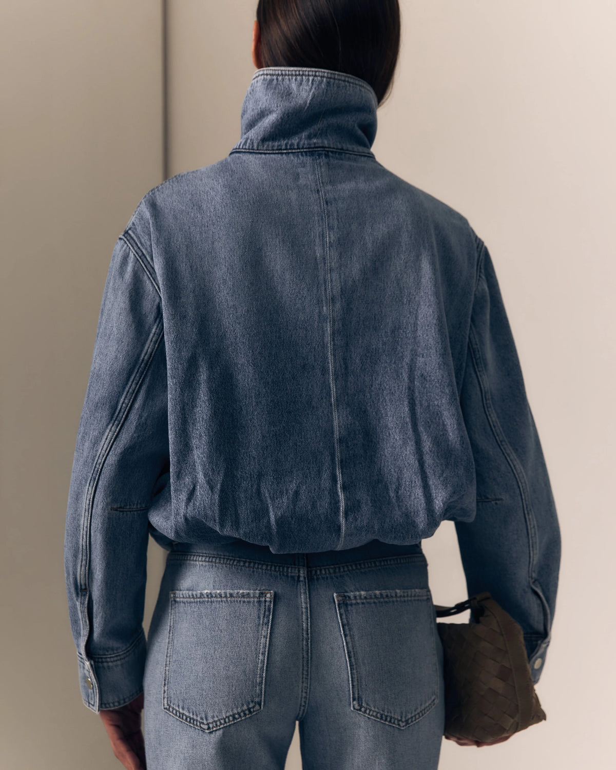 model wearing a denim jacket with jeans on a cream background, back view 