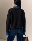 model wearing the harvey sweater that is a brown ribbed sweater with denim collar and cuff trim with jeans on a cream background, back view