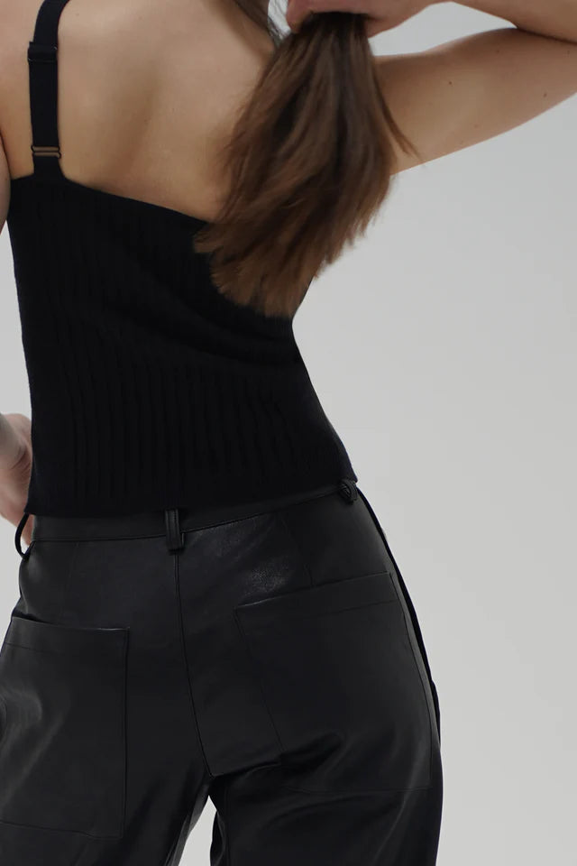 Person wearing a black ribbed tank top and black pants against a plain background back view