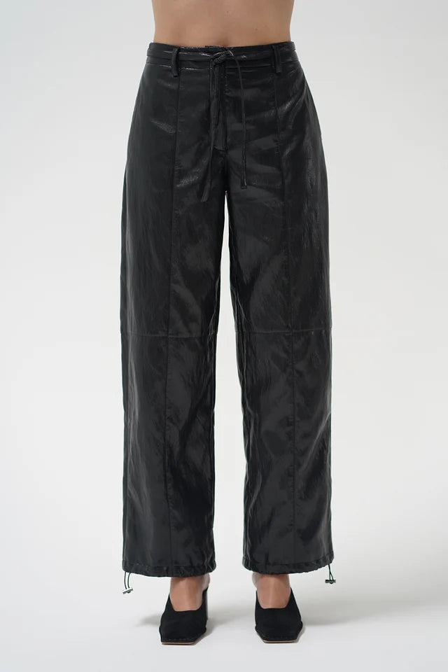 Black wide-leg pants with a glossy, slightly wrinkled texture, featuring a drawstring waist and drawstring hems, shown on a model against a light gray background.