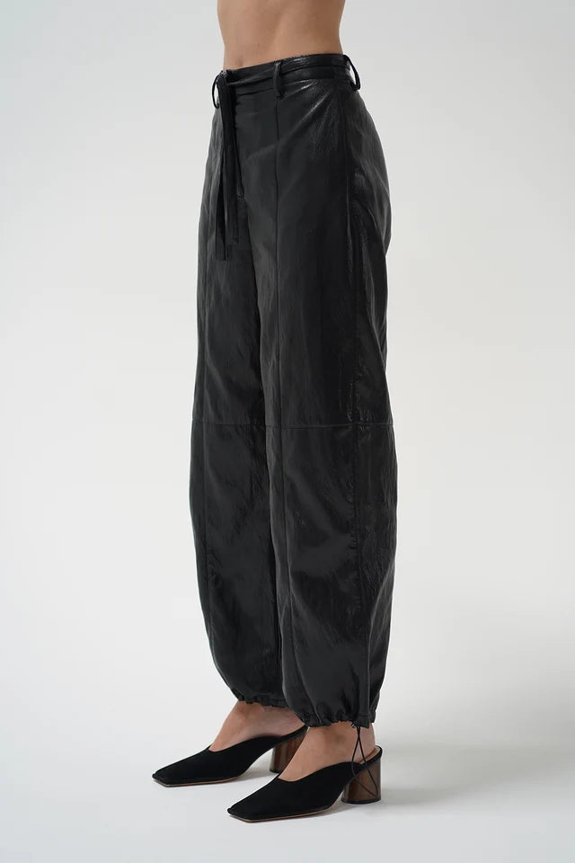 A model is shown from the waist down wearing black wide-leg harem pants with a drawstring waist and black mule heels, set against a plain light gray studio background.