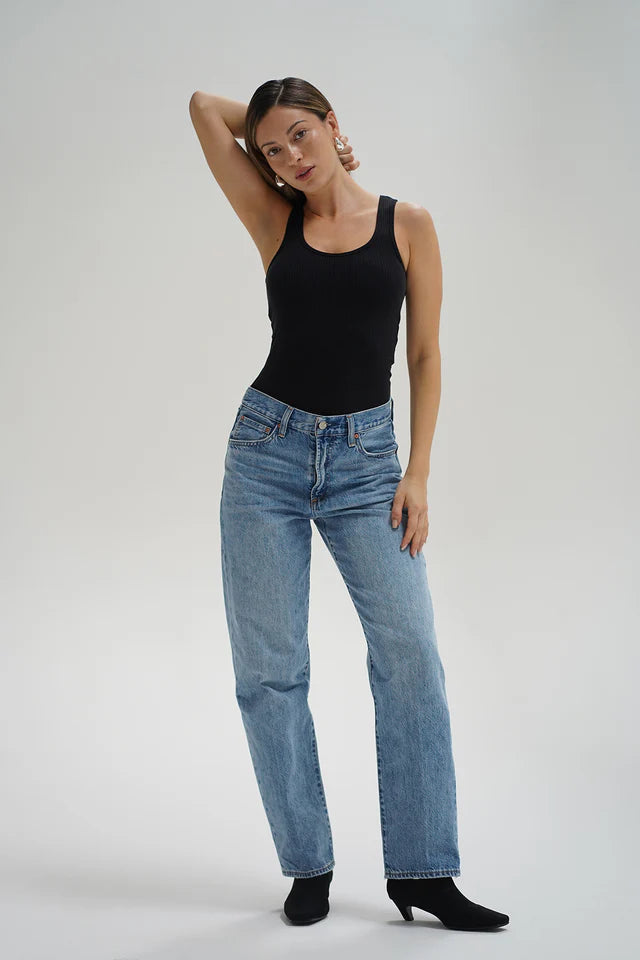 Woman wearing a black tank top and blue jeans on a plain background front view