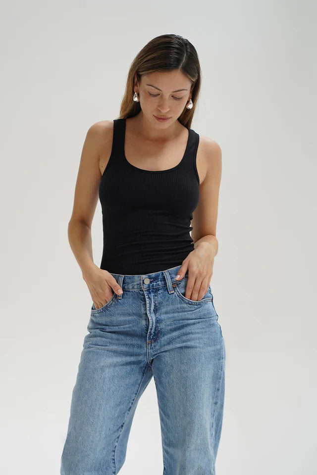 Woman wearing a black tank top and blue jeans against a plain background front view