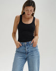 Woman wearing a black tank top and blue jeans against a plain background front view