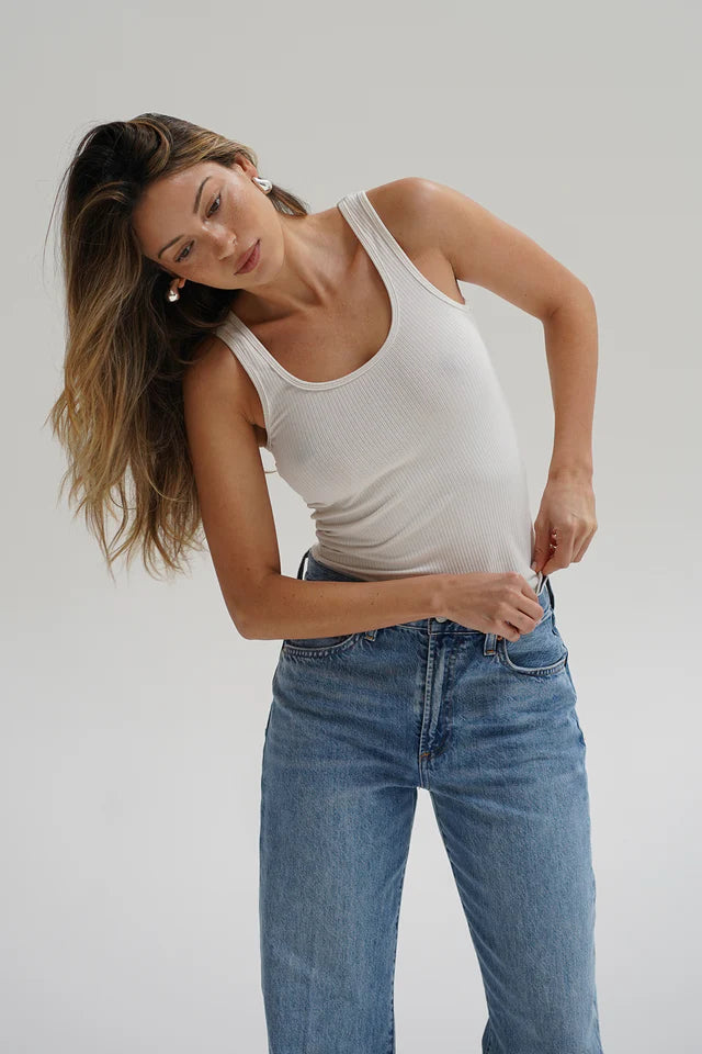 Woman wearing a white tank top and blue jeans against a plain background