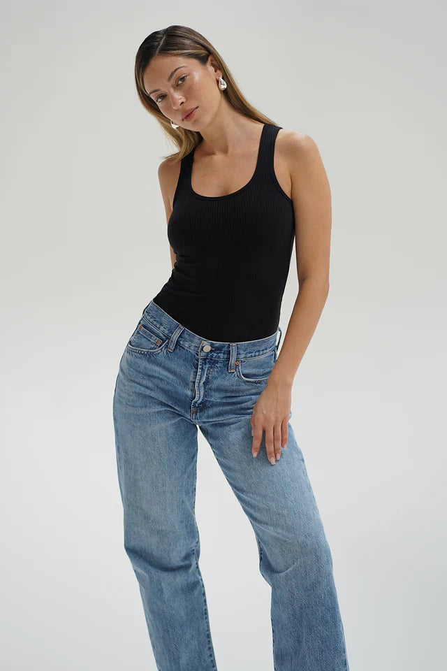 Woman wearing a black tank top and blue jeans on a plain background front view