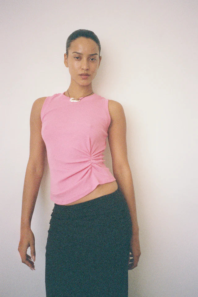 Woman wearing a pink sleeveless top and green skirt against a plain background