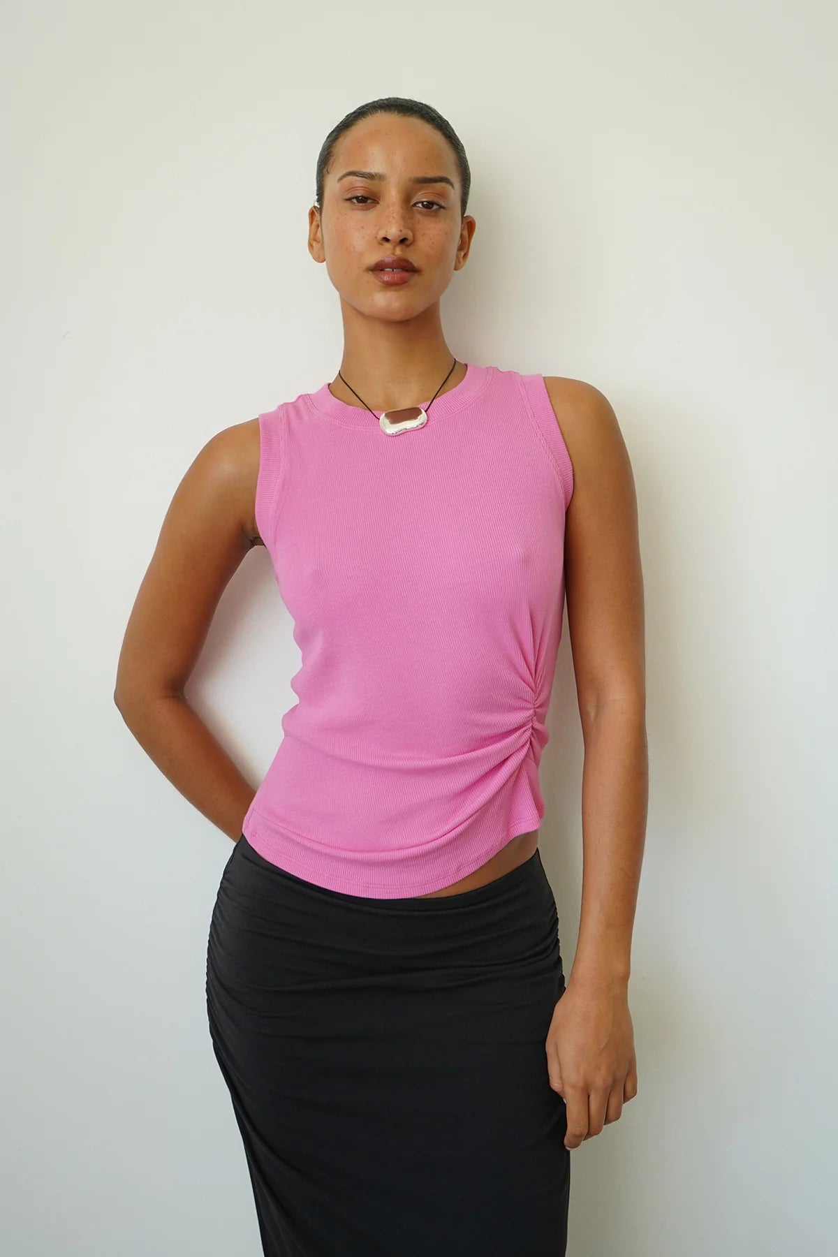Person wearing a pink sleeveless top and black skirt against a white background