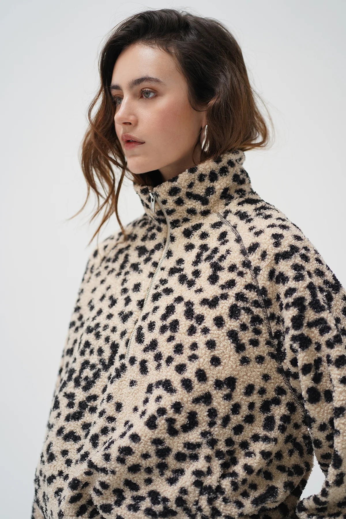 A woman wearing a beige sherpa fleece jacket with a black leopard print pattern, photographed against a plain light gray studio background.