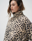 A woman wearing a beige sherpa fleece jacket with a black leopard print pattern, photographed against a plain light gray studio background.