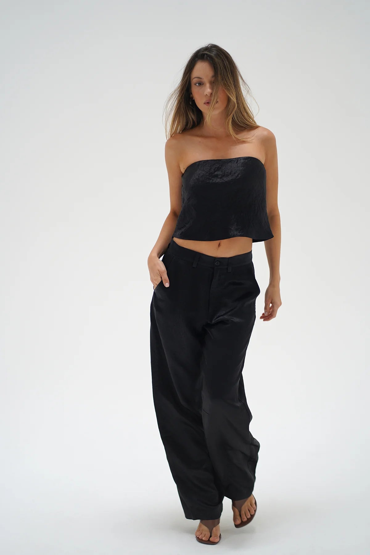 Woman wearing a black strapless top and wide-leg pants on a white background