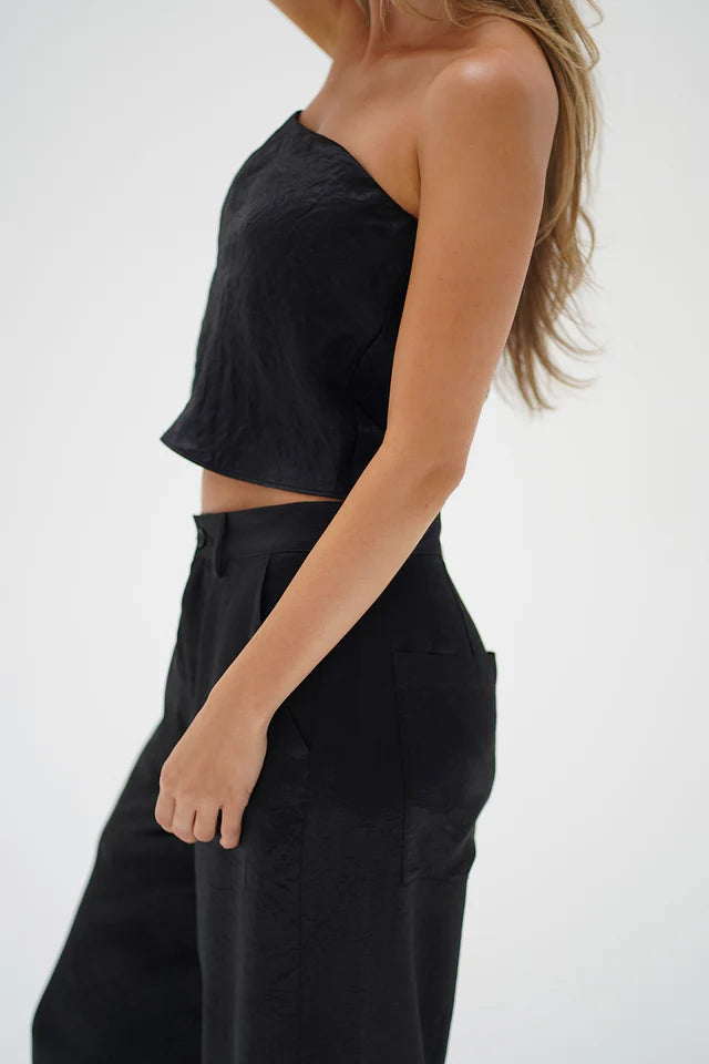 Person wearing a black one-shoulder top and black pants on a white background