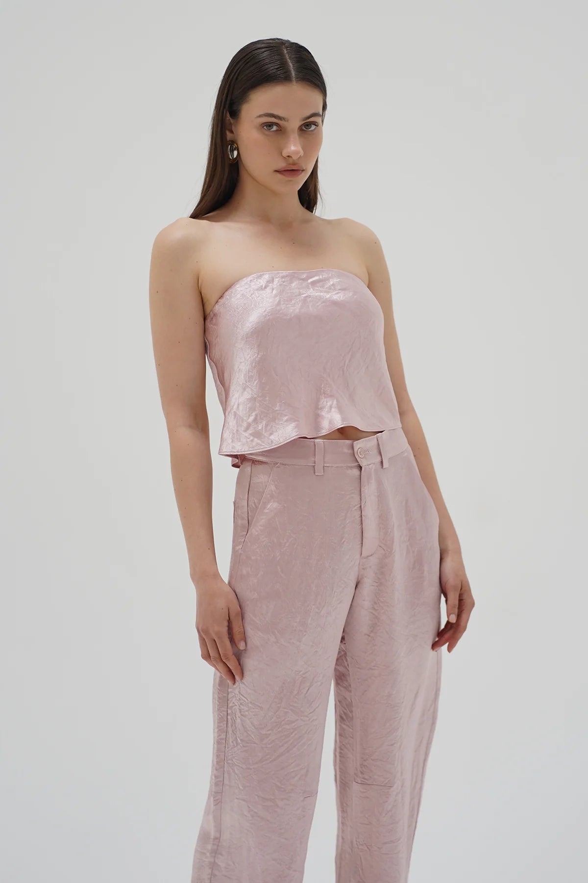 Woman wearing a pink strapless top and pants on a light gray background