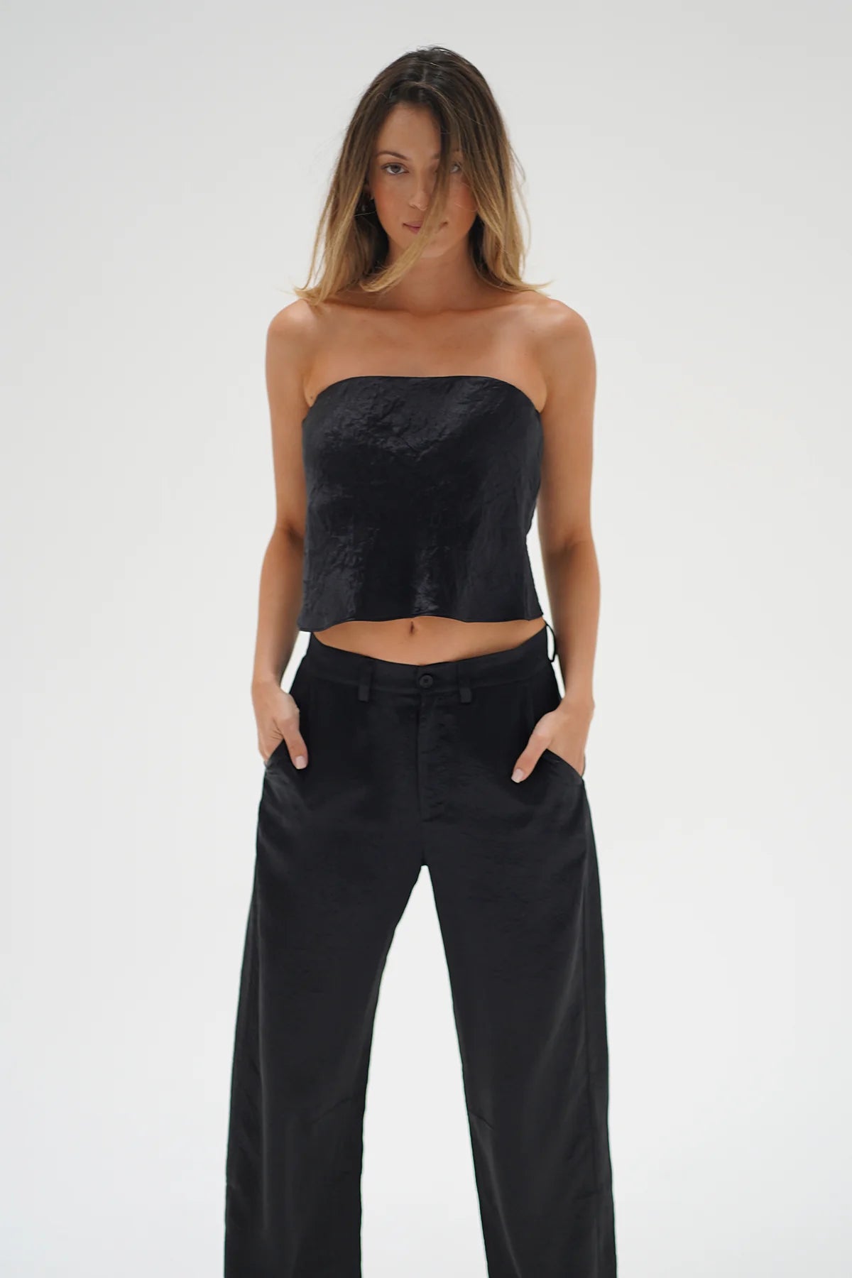 Woman wearing a black strapless top and black pants on a white background