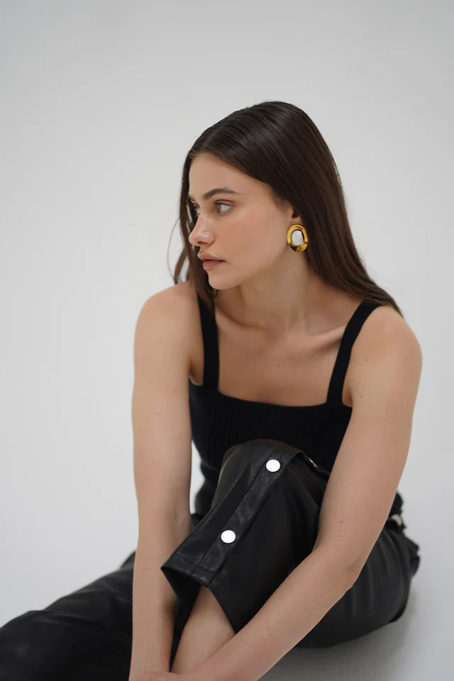 Woman wearing a black dress with silver buttons against a white background front view