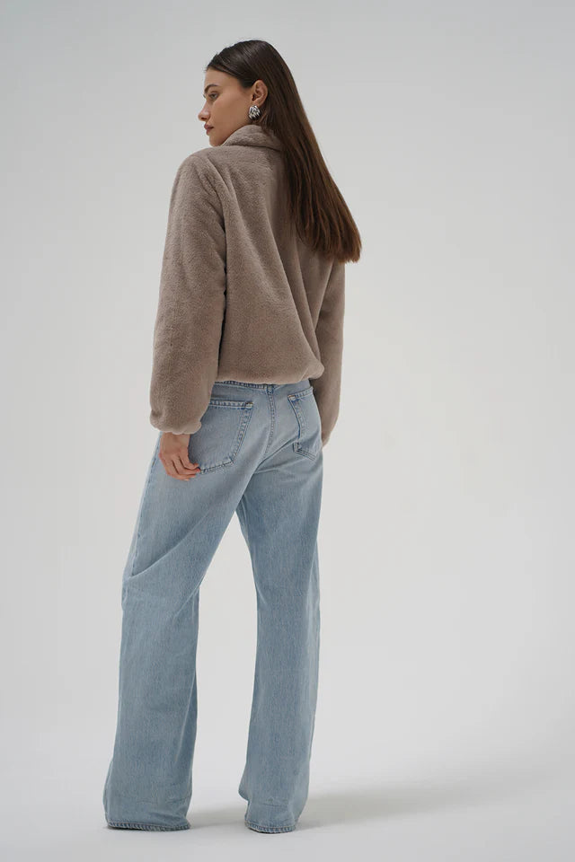 Person wearing a brown fleece jacket and light blue jeans on a plain background