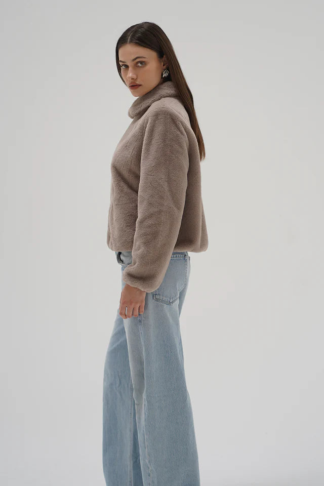 Woman wearing a beige sweater and light blue jeans on a plain background