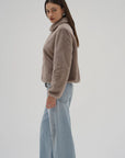 Woman wearing a beige sweater and light blue jeans on a plain background