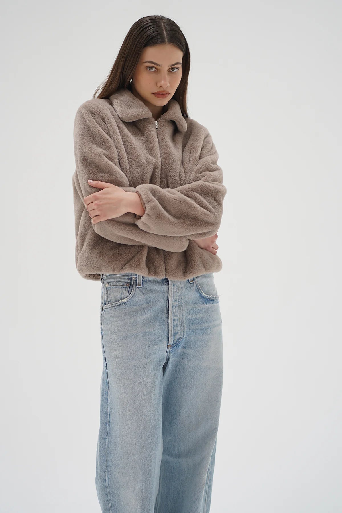 Woman wearing a brown sweater and light blue jeans on a white background
